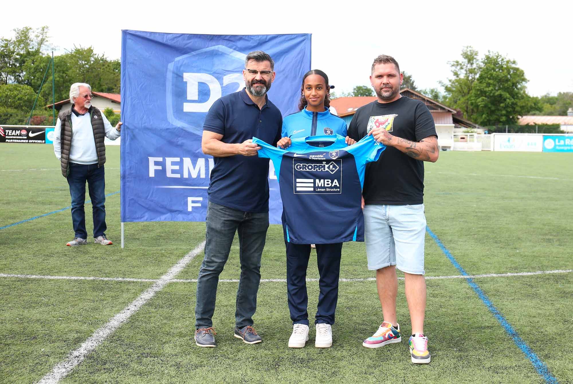 Remise de maillot de foot à une joueuse par deux hommes sur terrain